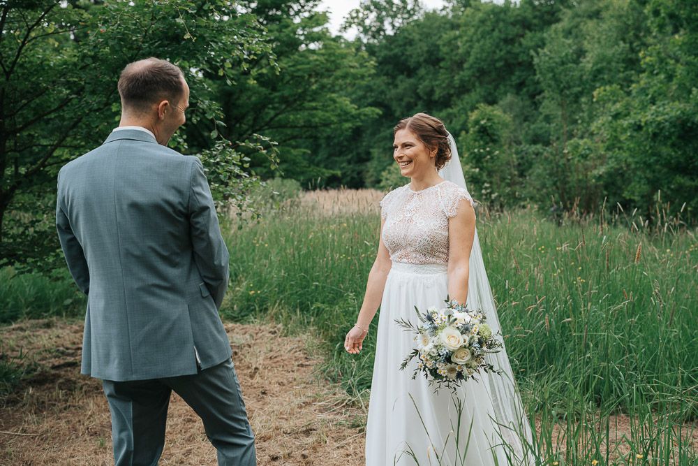 Couple shares a joyful moment on a dirt path surrounded by lush greenery and wildflowers during a countryside wedding.