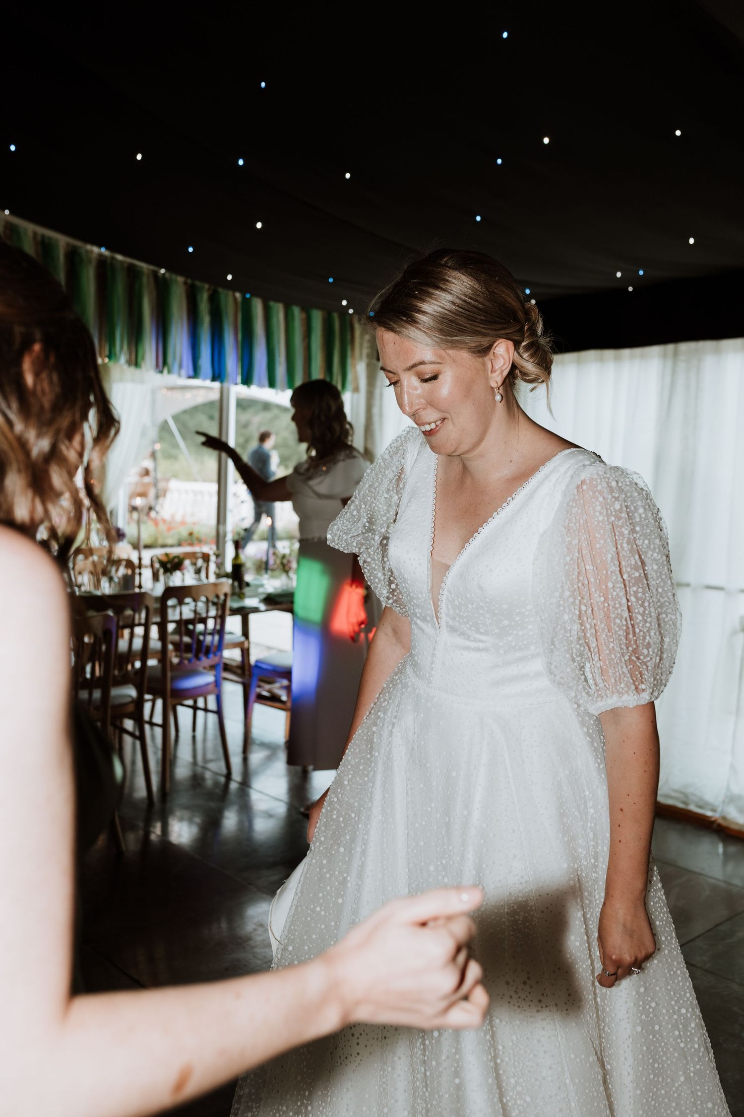 A sequence showing someone adjusting a flowing white wedding dress with delicate short lace sleeves in a dimly lit venue.