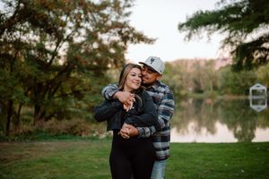 A tender family photo session outdoors in a park with autumn trees and a lake in the background.