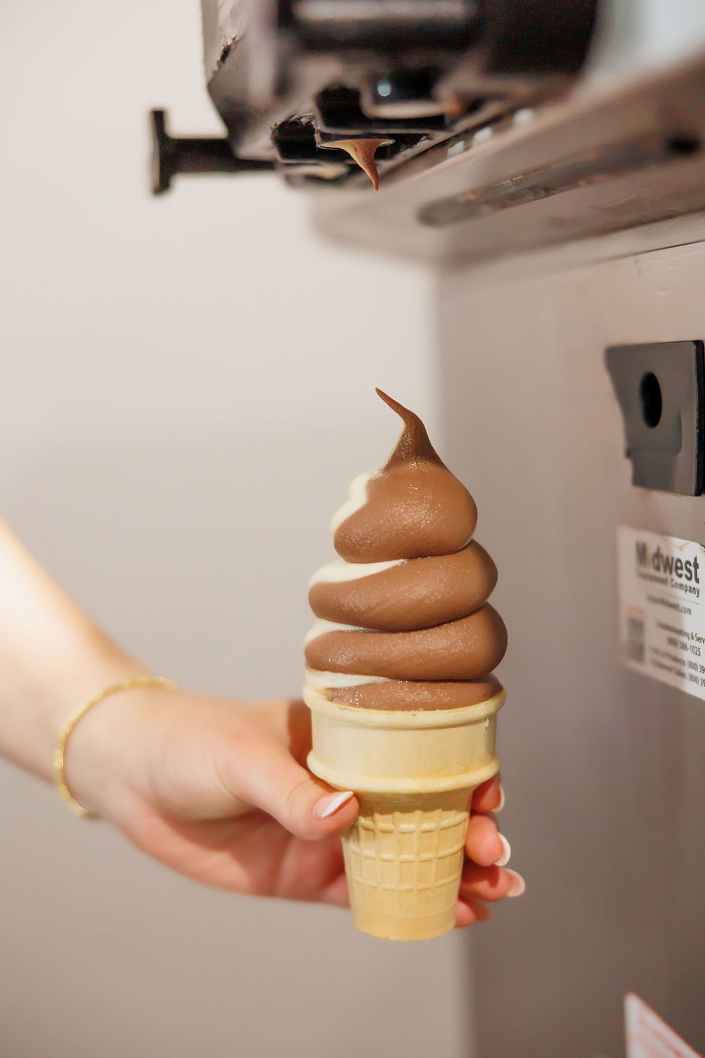 A chocolate soft serve ice cream swirled perfectly into a wafer cone held by a hand.