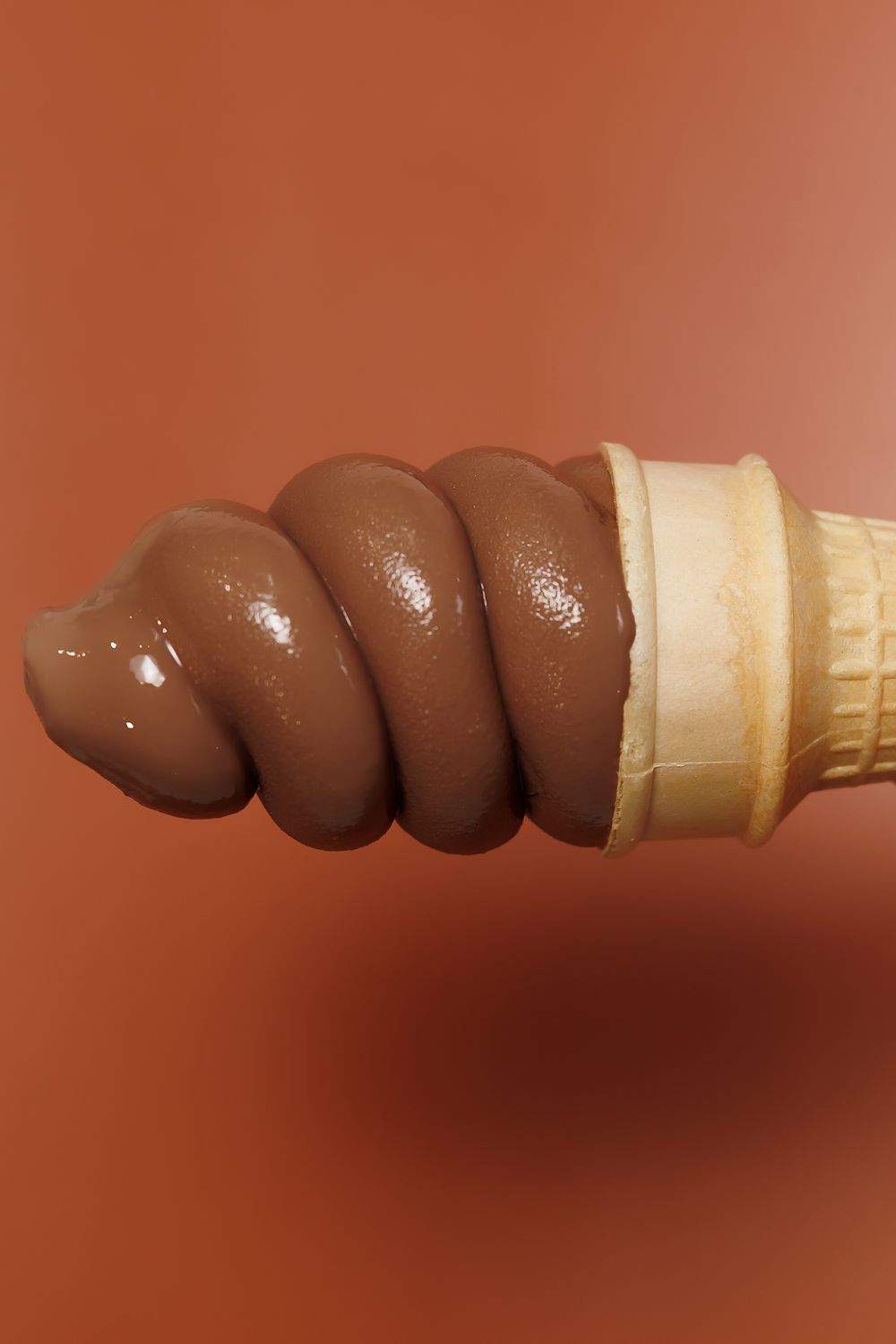 Chocolate ice cream scoops arranged in a spiral pattern on a wafer cone against brown background.