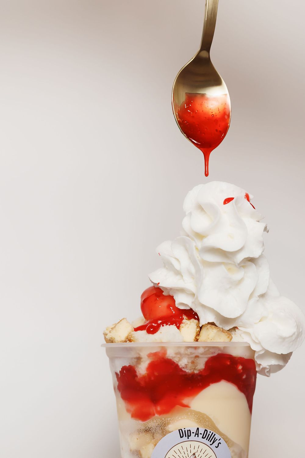 Red syrup being poured over whipped cream sundae topped with fresh berries.