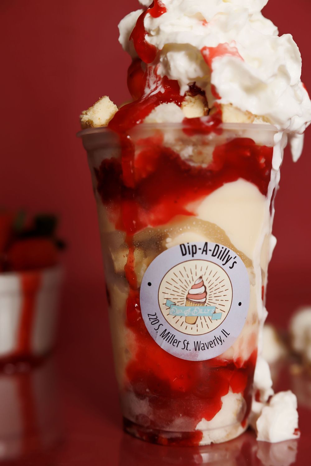 Decadent ice cream sundae with whipped cream and red syrup in a Dip-A-Dillas branded cup.
