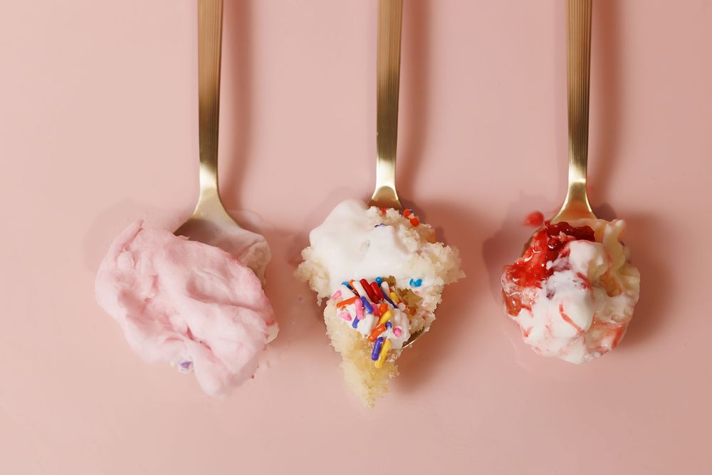 Row of ice cream cones topped with pink cream and colorful sprinkles on pink surface.