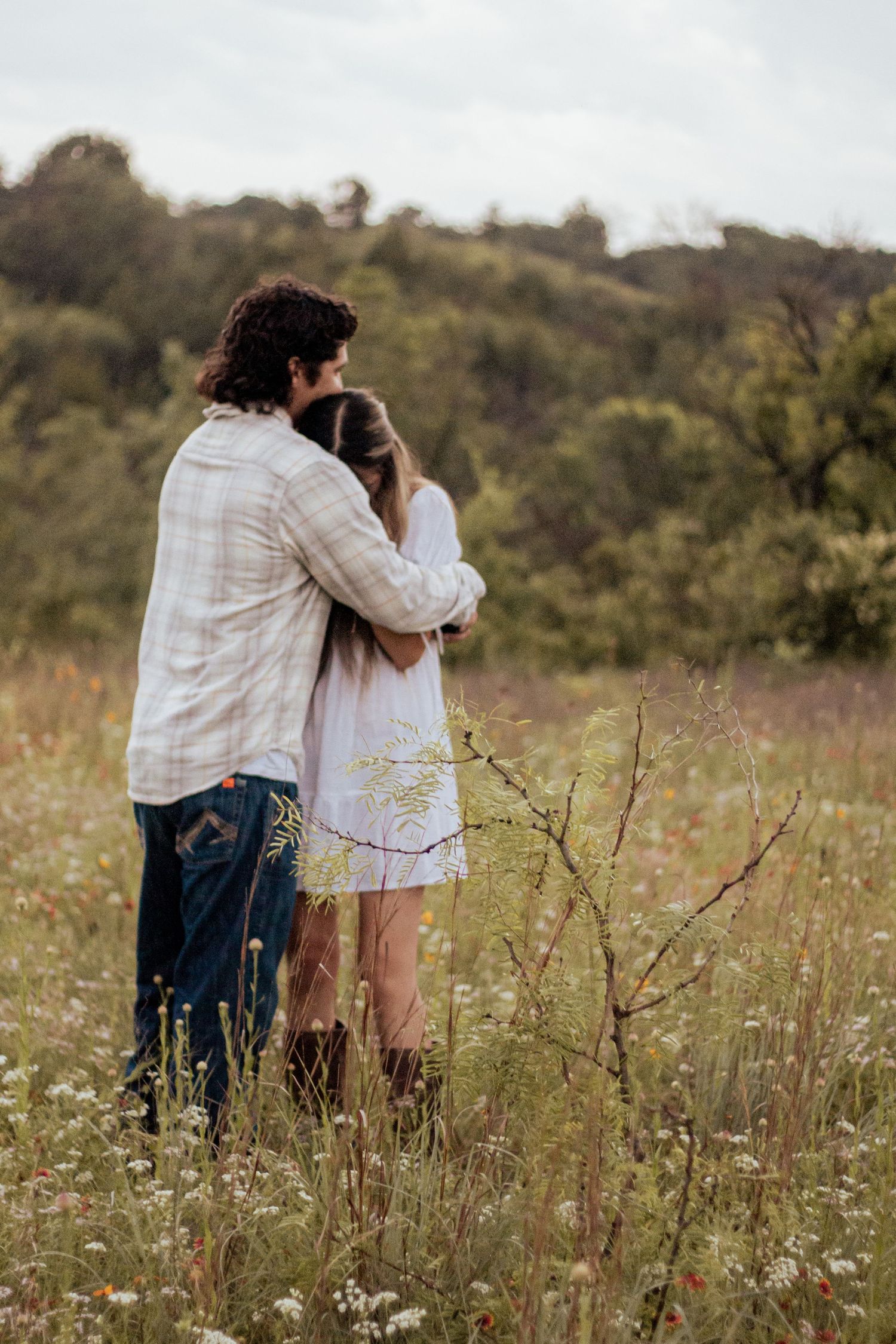 Two people sitting together in a wildflower meadow at sunset sharing intimate moments among blooming white flowers.