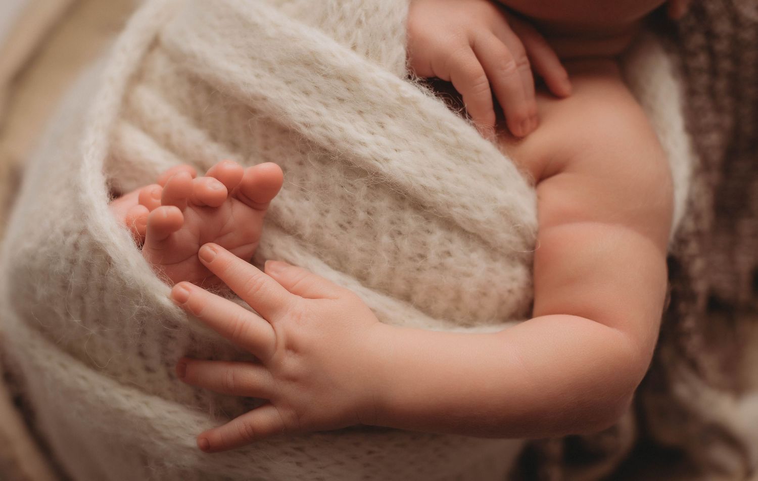 Small bare feet peek out from beneath a soft white knit blanket, creating a tender and intimate moment.