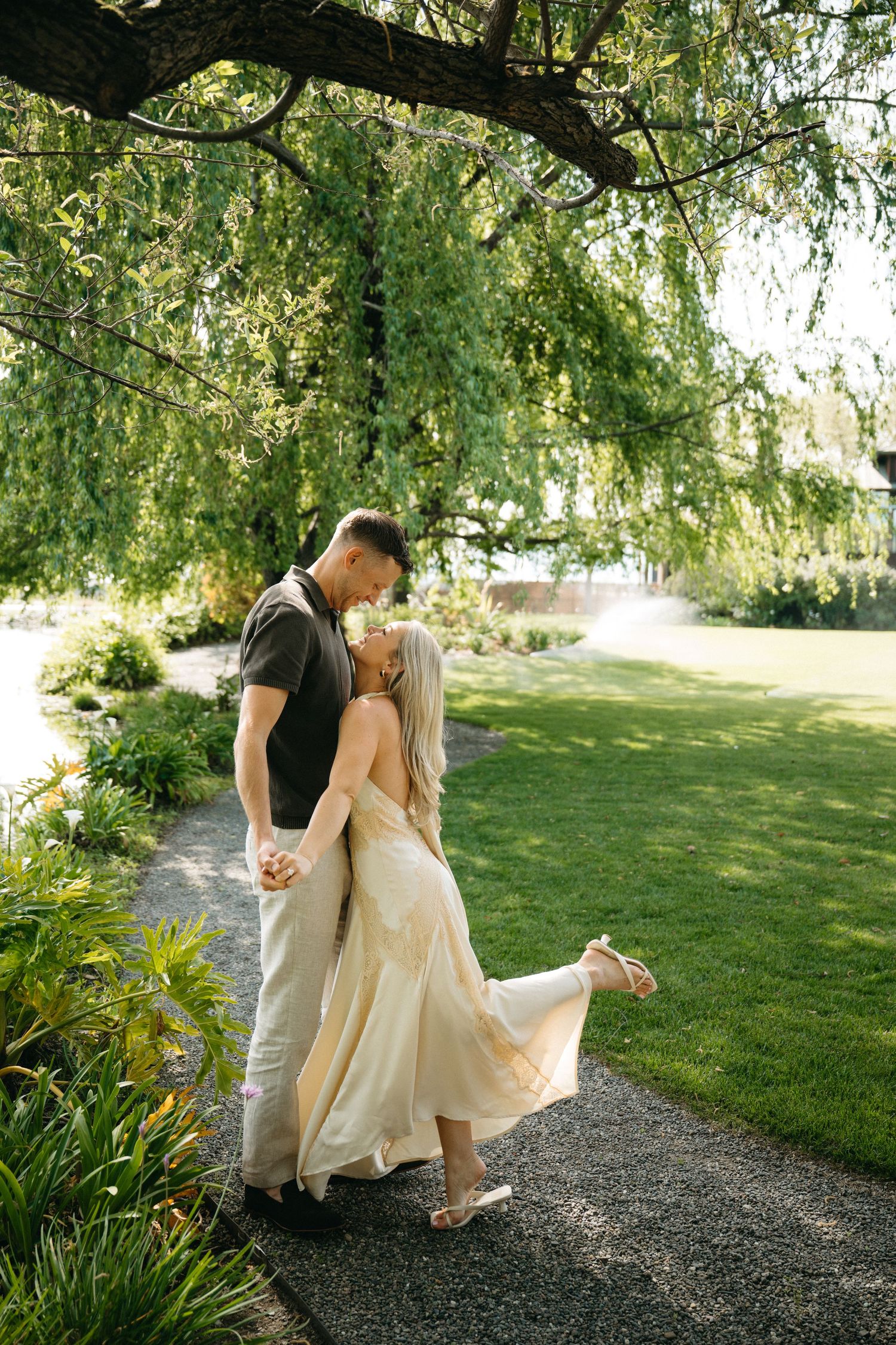 Couple in western-inspired outfits poses against rustic wooden wall with the woman wearing white dress and boots.