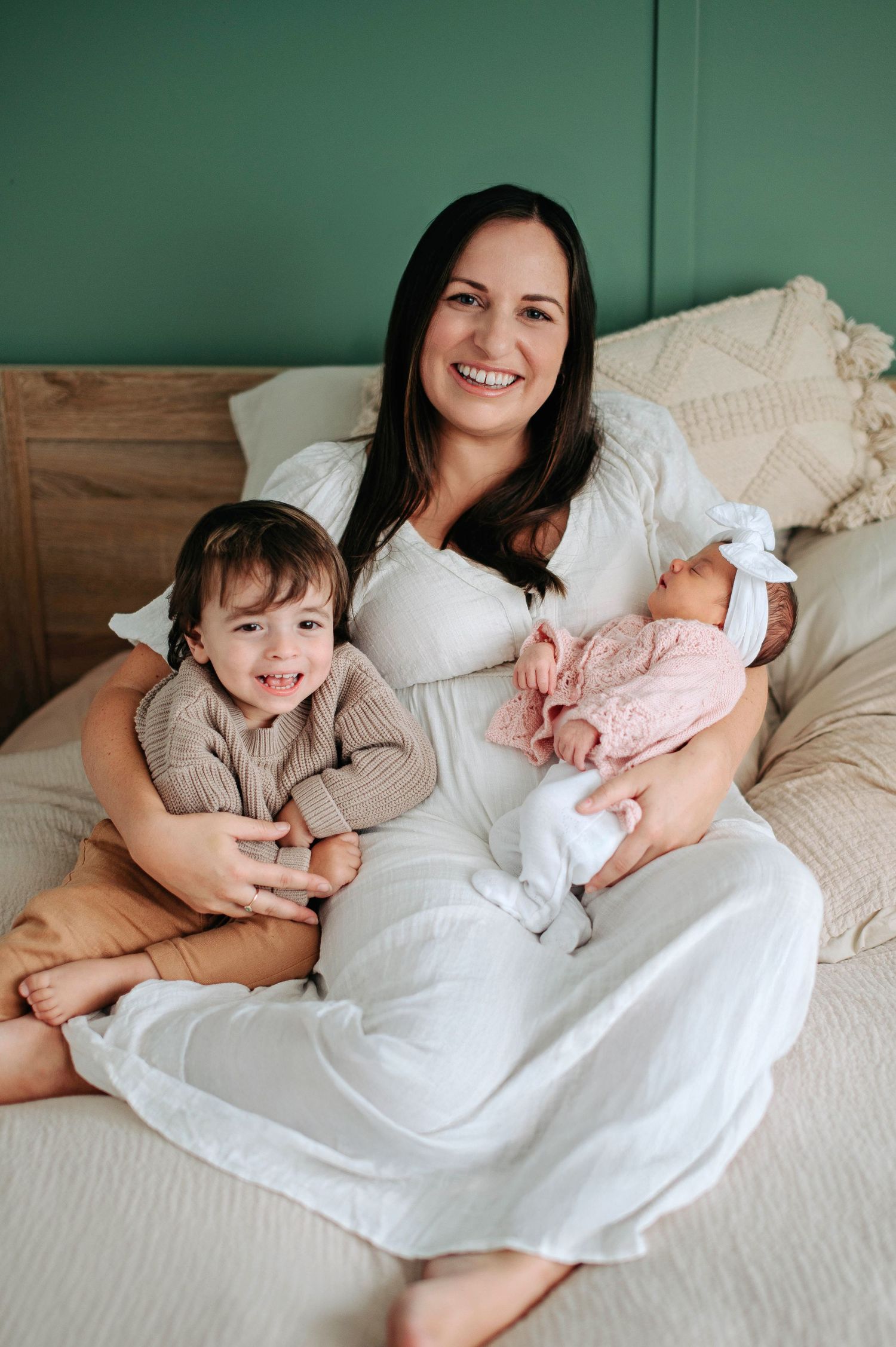 A family sitting together on a cozy bed with white linens against a green wall, sharing a tender moment.