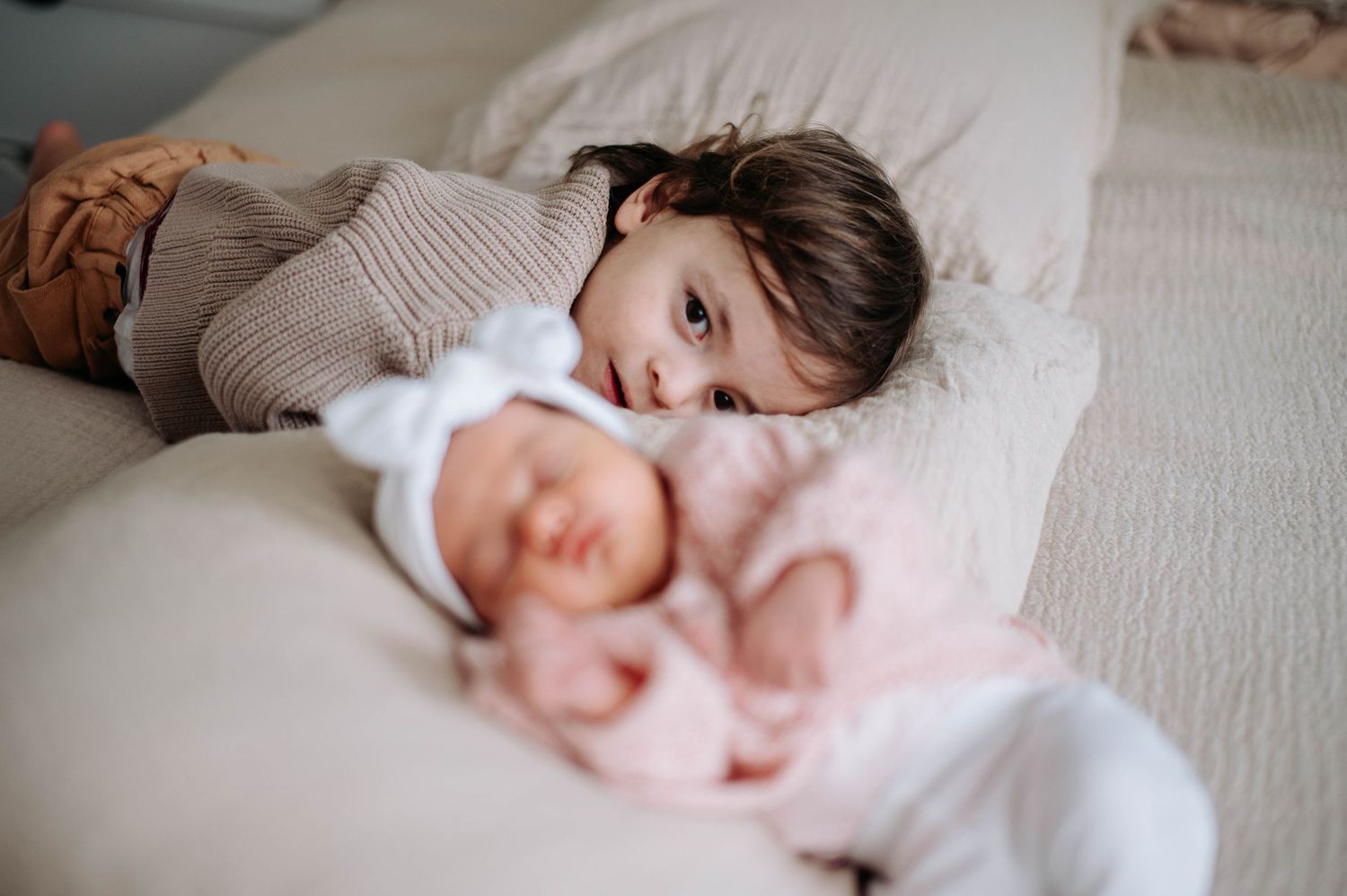 A child rests peacefully on white bedding while snuggling a soft pink plush toy.
