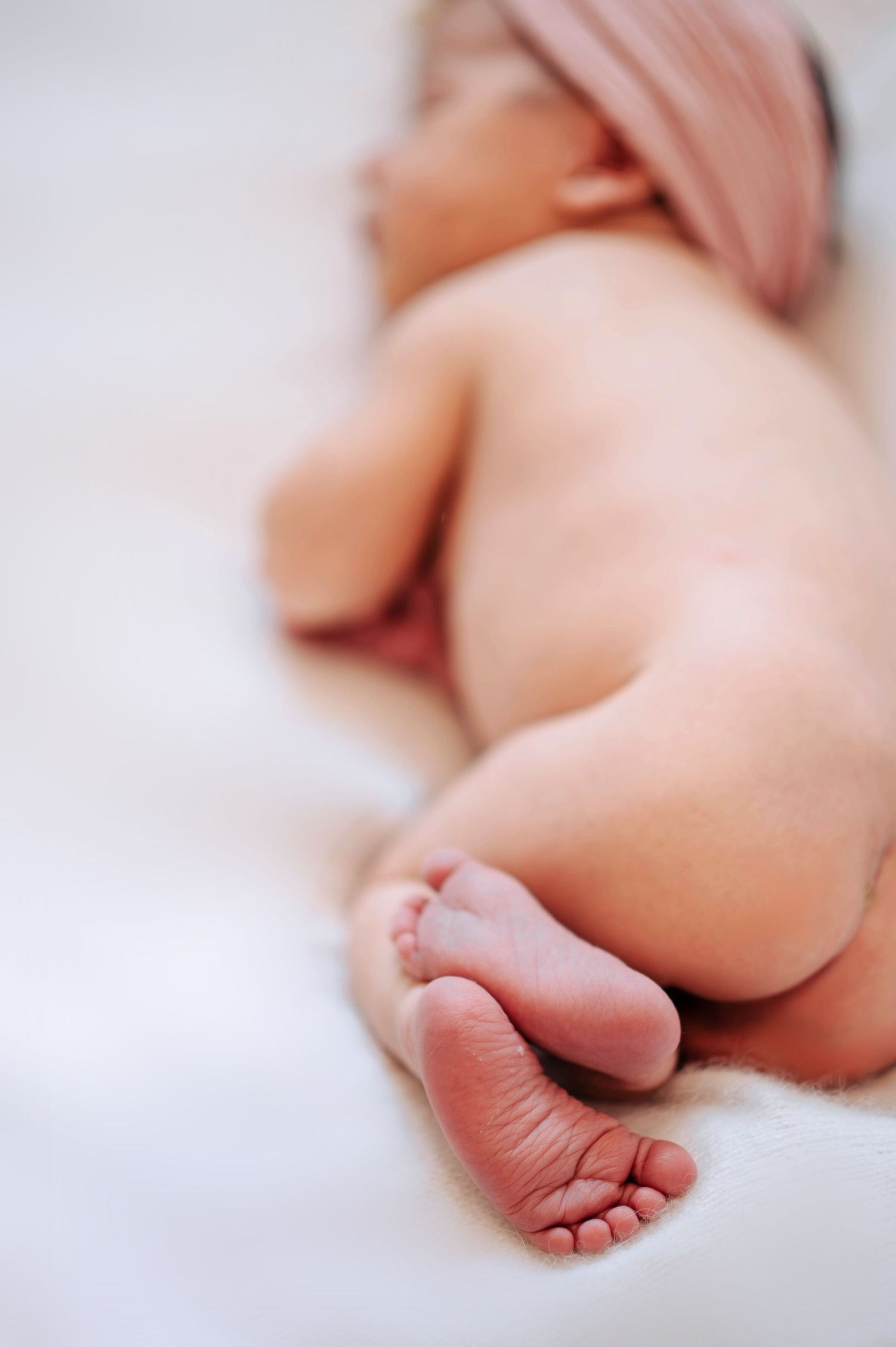 Close-up photograph of tiny newborn baby feet against white bedding in soft natural light.