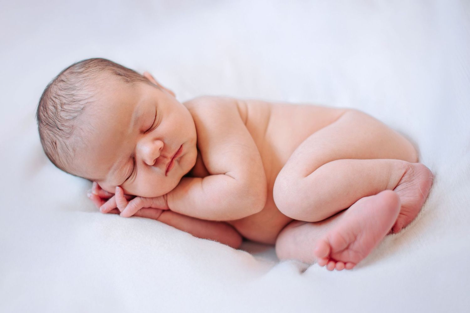 A series of four soft, peaceful photographs showing a sleeping newborn baby in various gentle poses on white fabric.