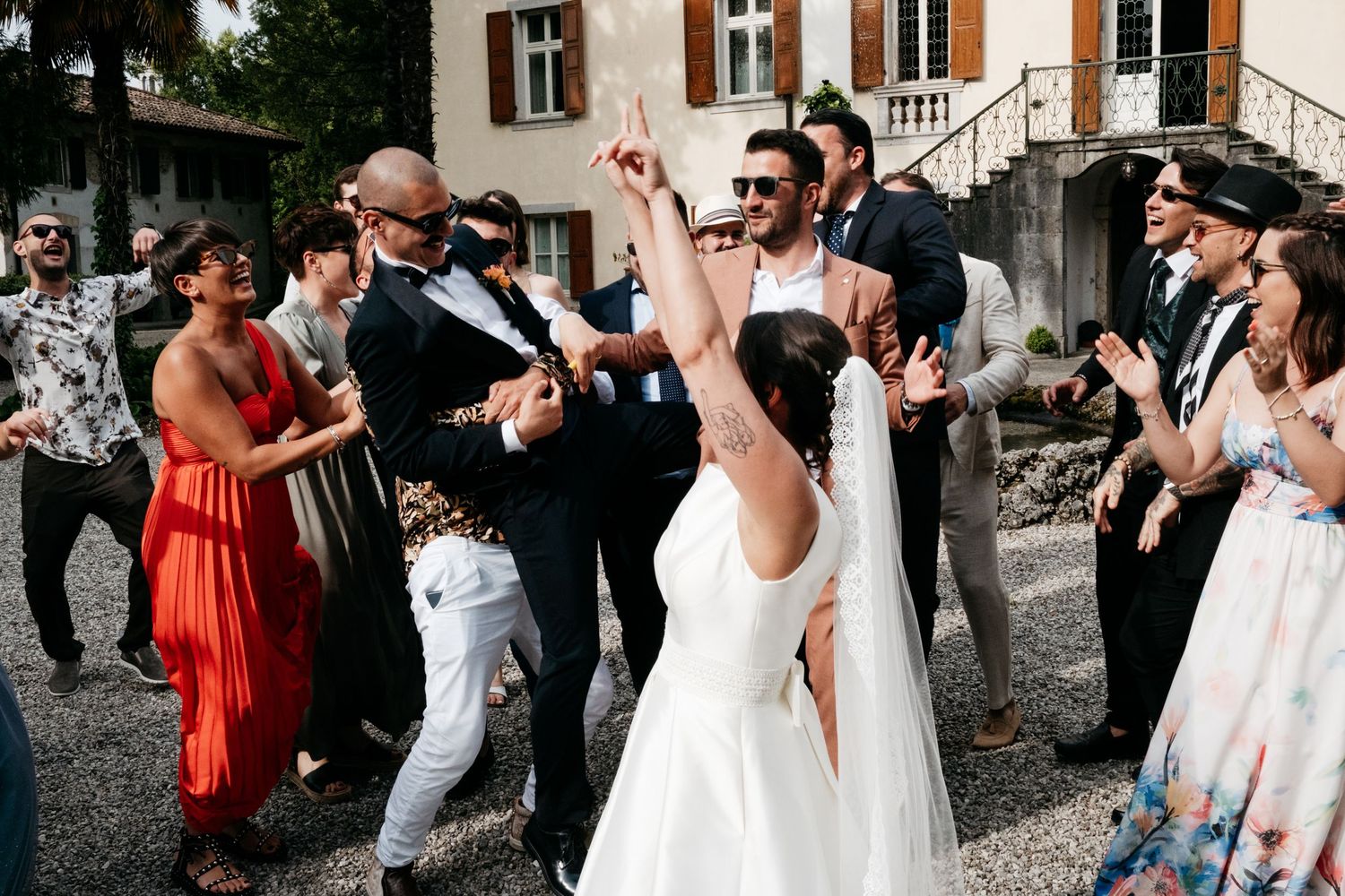 Black and white photo of energetic wedding guests celebrating and dancing outdoors at a daytime reception.