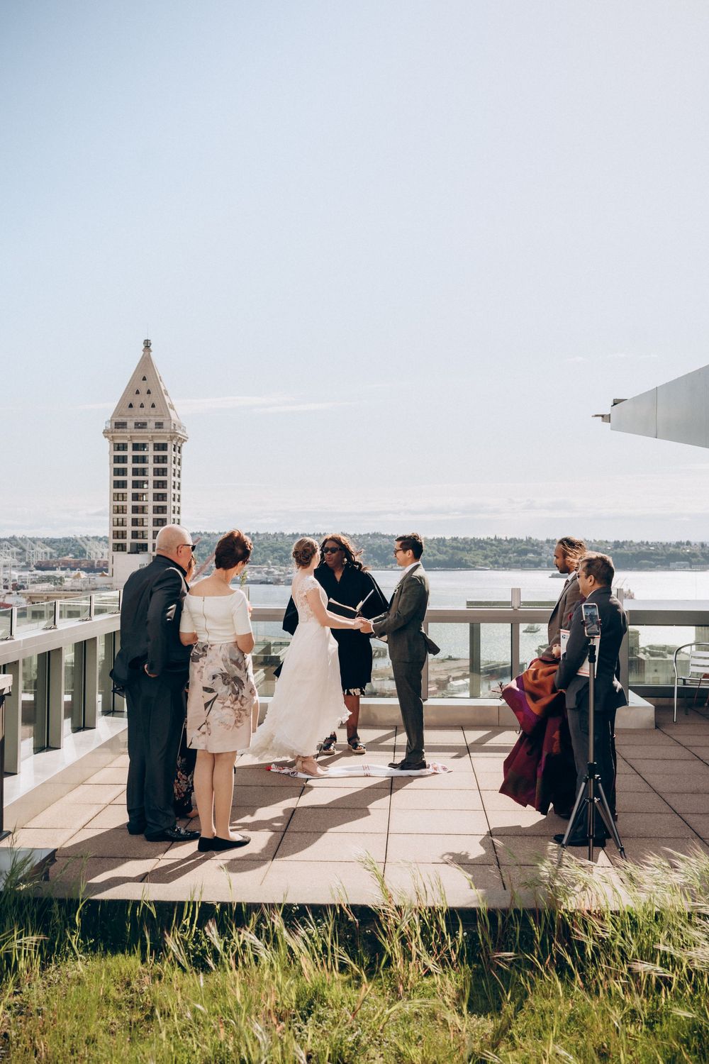 Intimate rooftop wedding ceremony taking place with Seattle Smith Tower and Elliott Bay visible in background.
