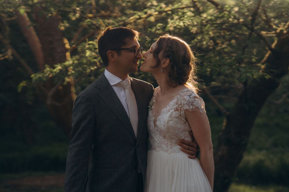 A couple embraces in an intimate moment against a sunlit garden backdrop wearing wedding attire.
