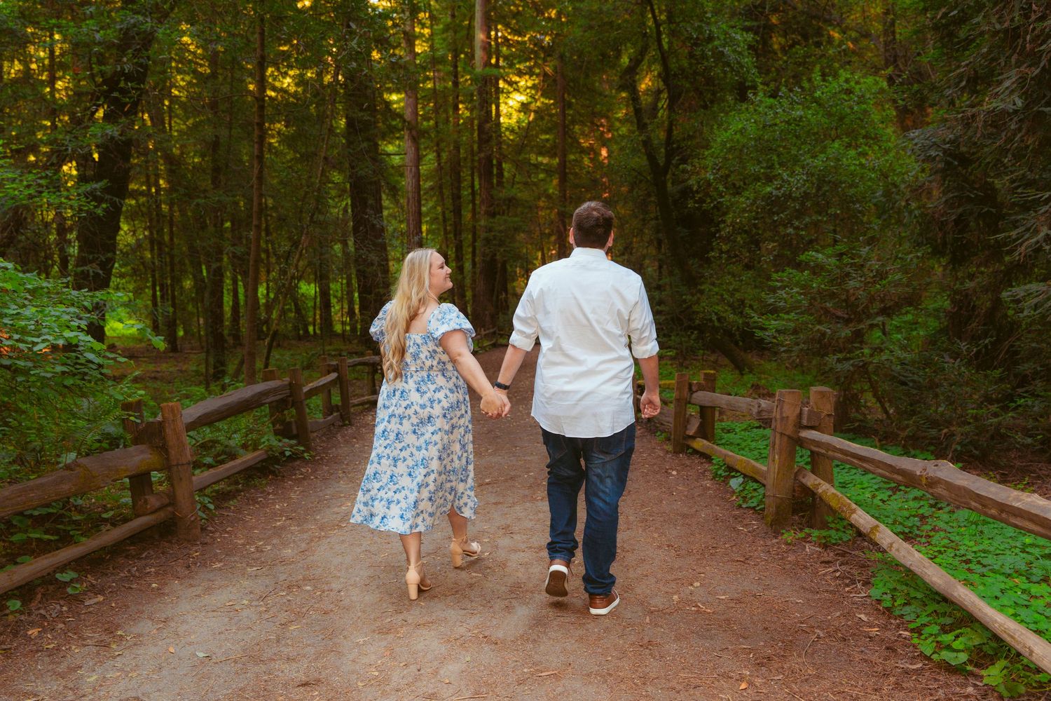 A couple enjoys a picnic on a blanket in a sunlit forest, pouring wine and relaxing together on a warm day.