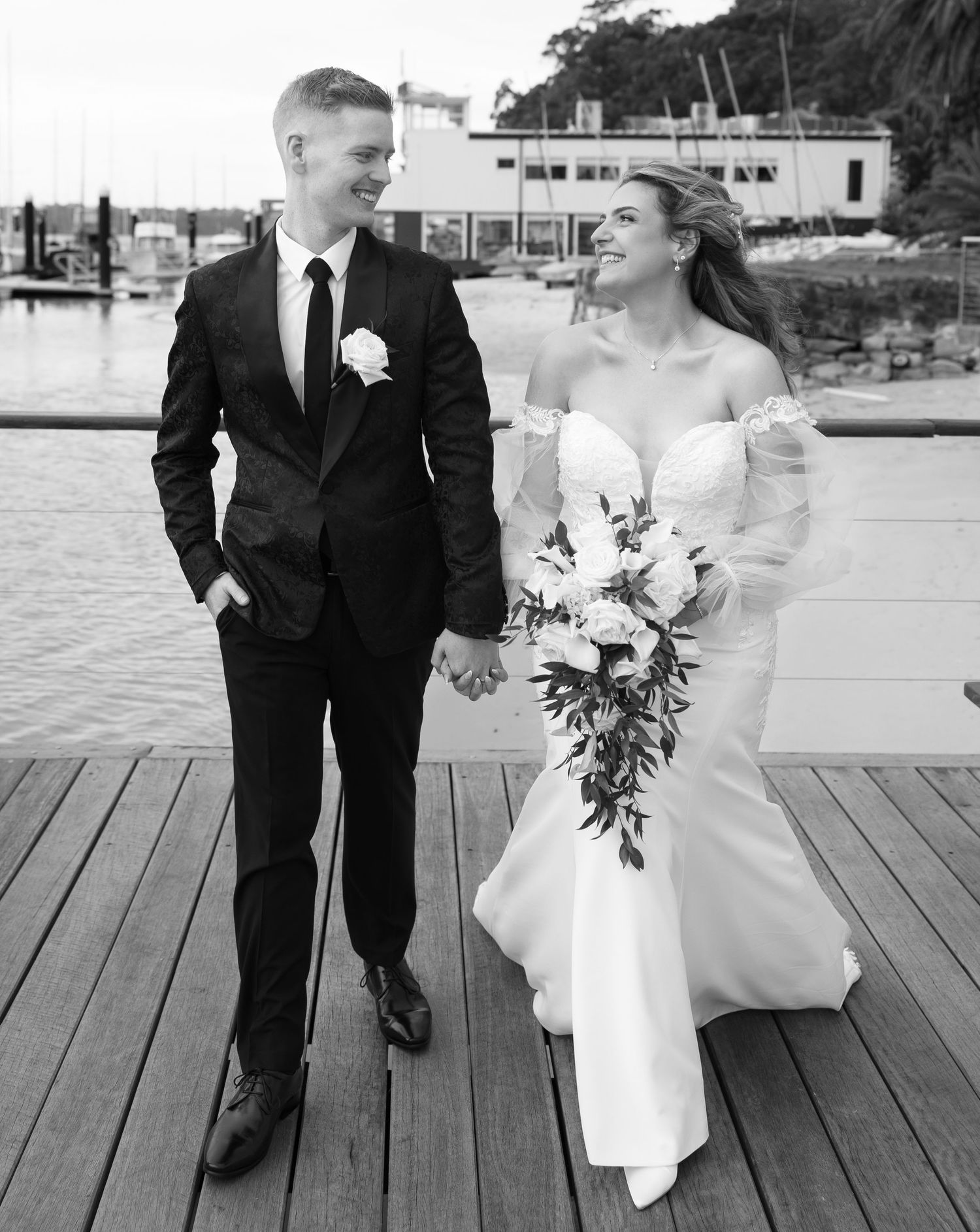 Intimate black and white wedding portrait of bride and groom embracing under veil with romantic gaze.