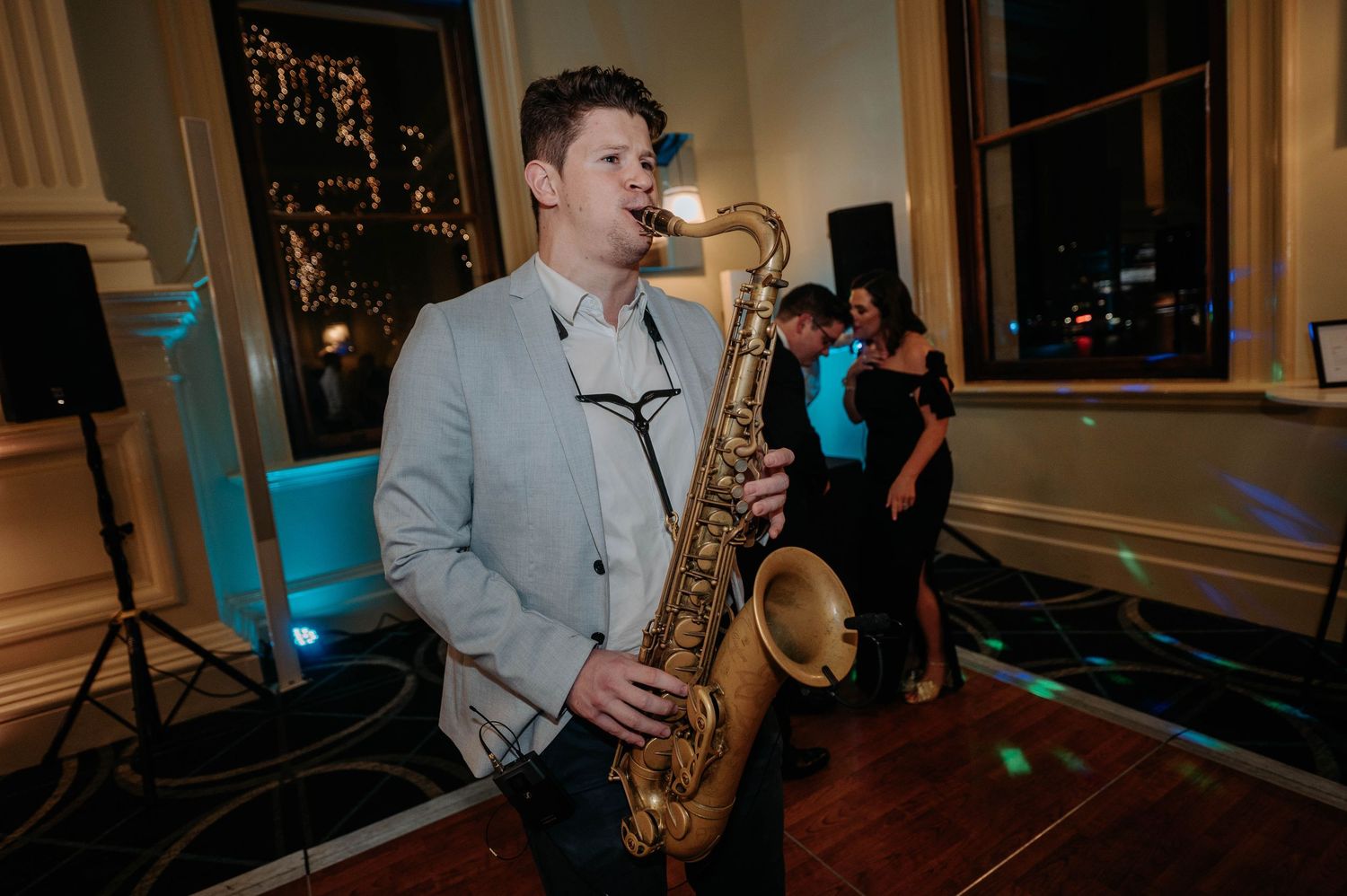 A saxophone player performs at an evening event in a brightly lit room with warm ambiance.