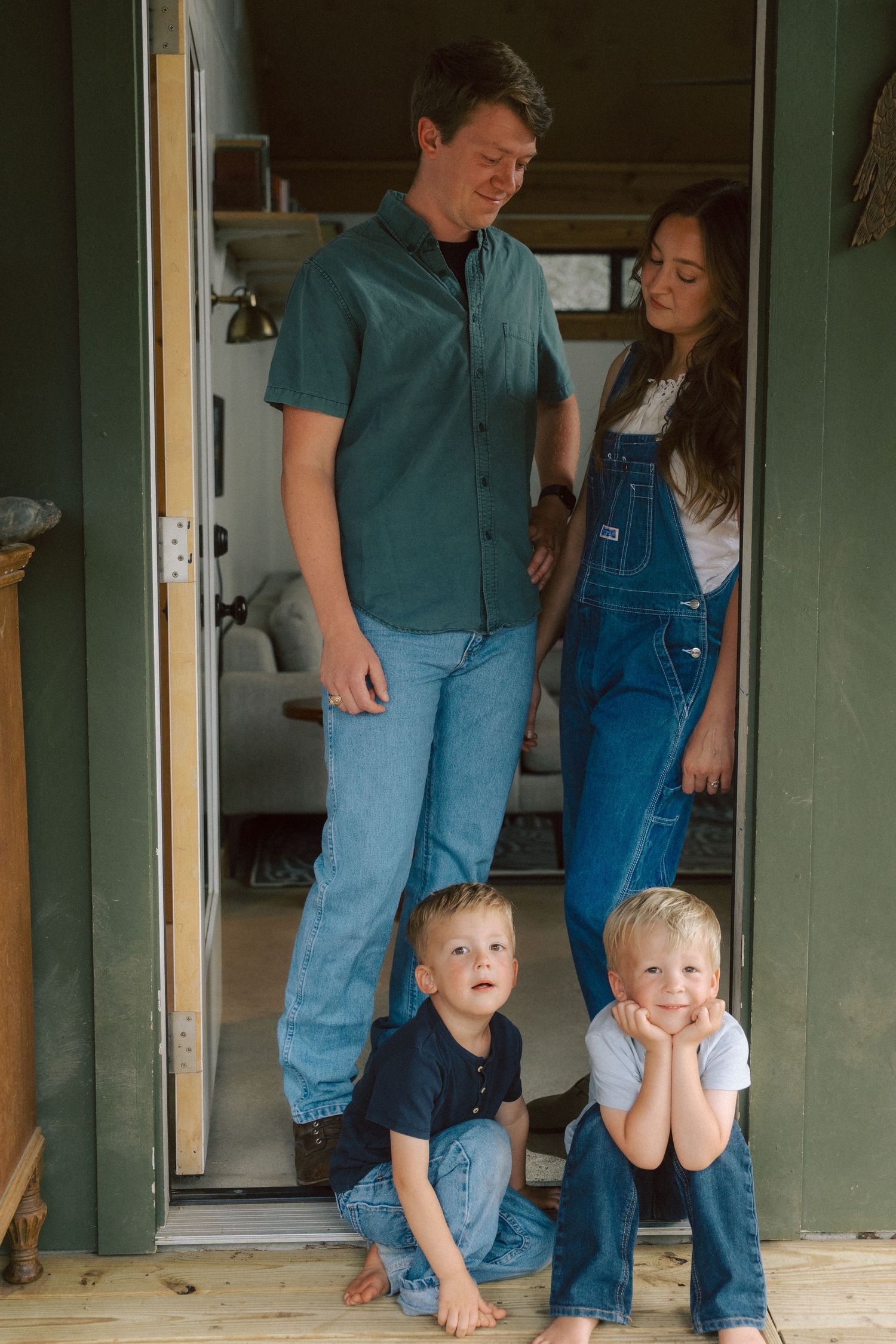 A family poses together in a rustic doorway wearing casual denim and teal clothing.