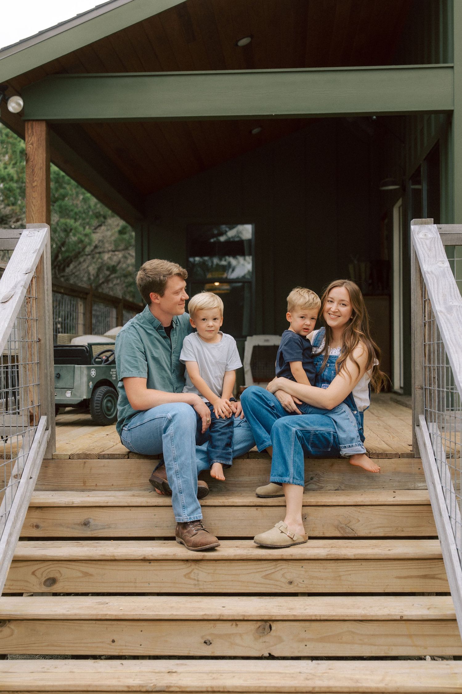 A family sits together on wooden steps of a rustic porch on a summer day.