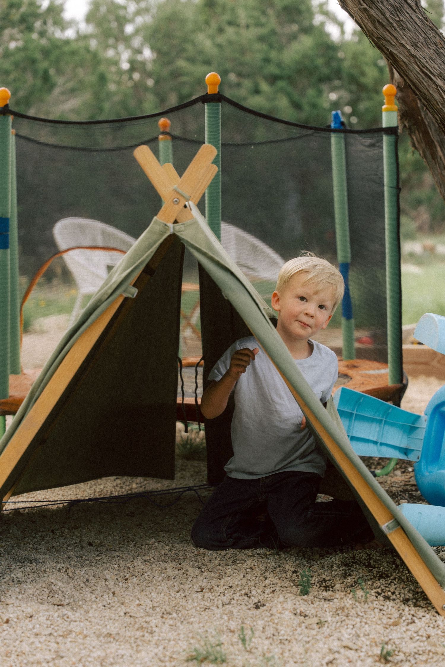 A small outdoor fort set up at a playground with canvas and wooden beams creates a cozy play space.