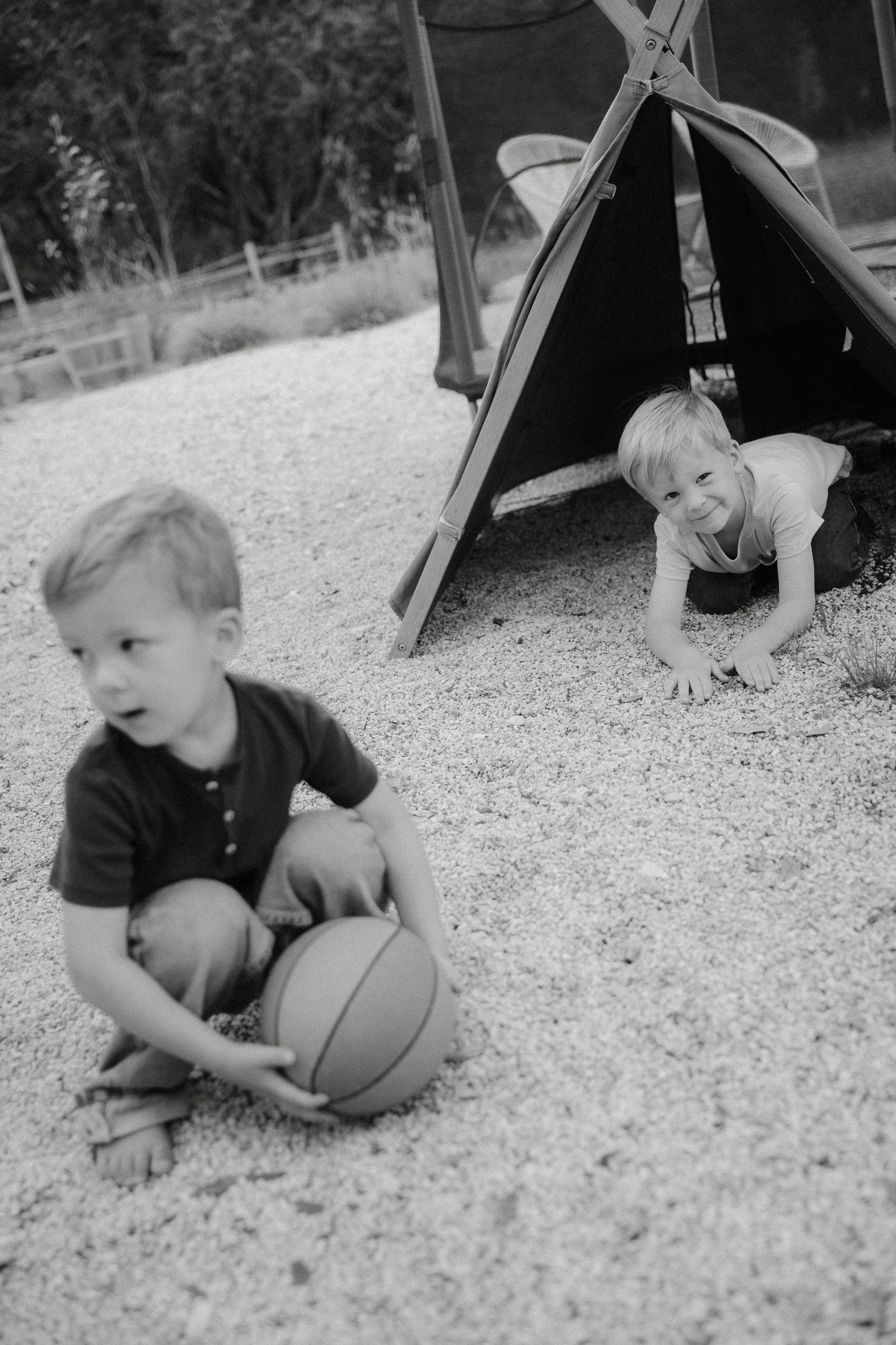 Black and white photo showing two children playing outdoors with a basketball and small tent structure.