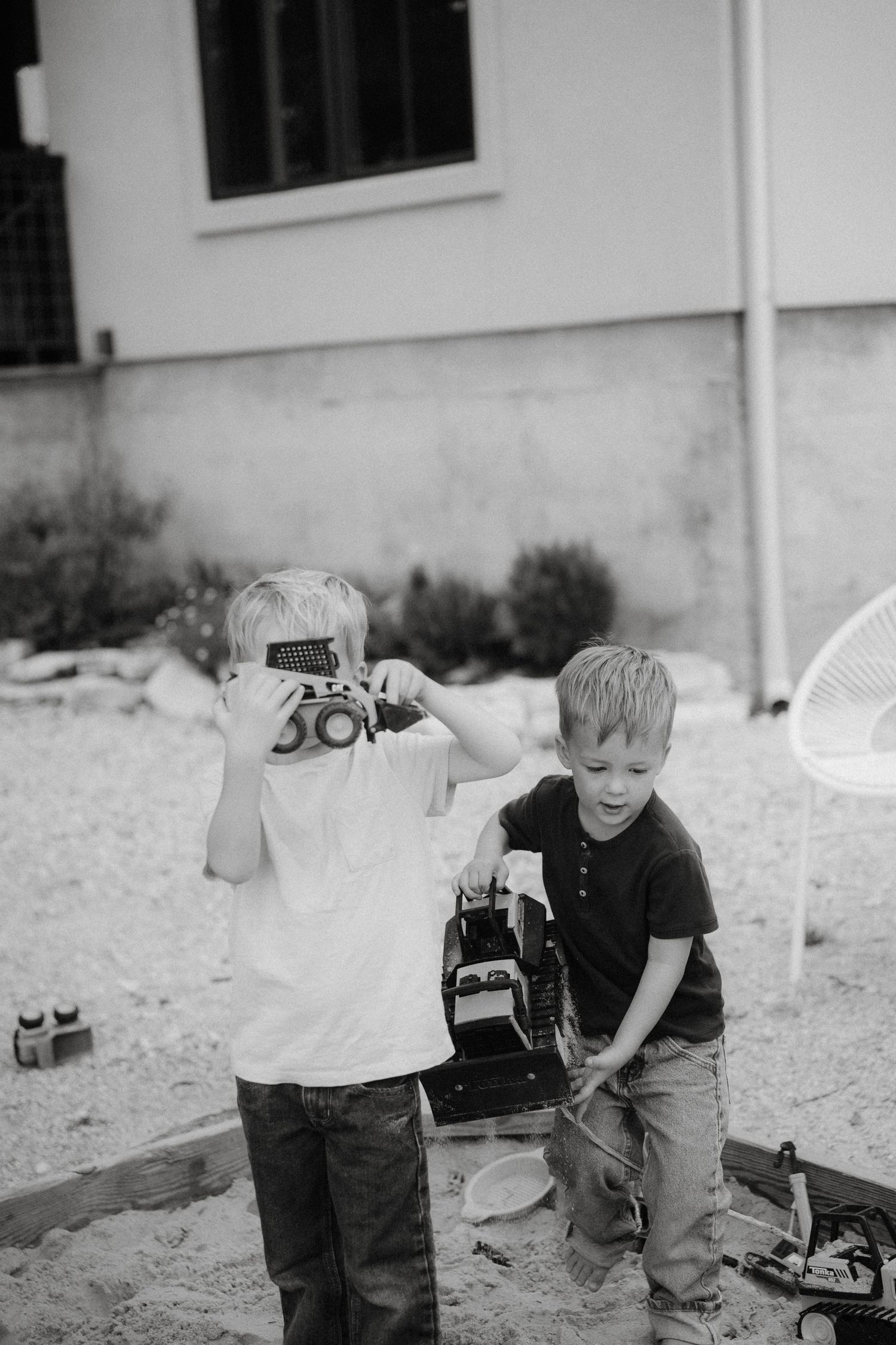 Two children playing together in a sandy outdoor area in black and white.