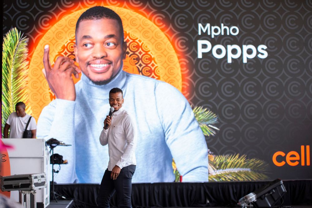 A person performs on stage against a large orange and black video wall display featuring promotional branding graphics.