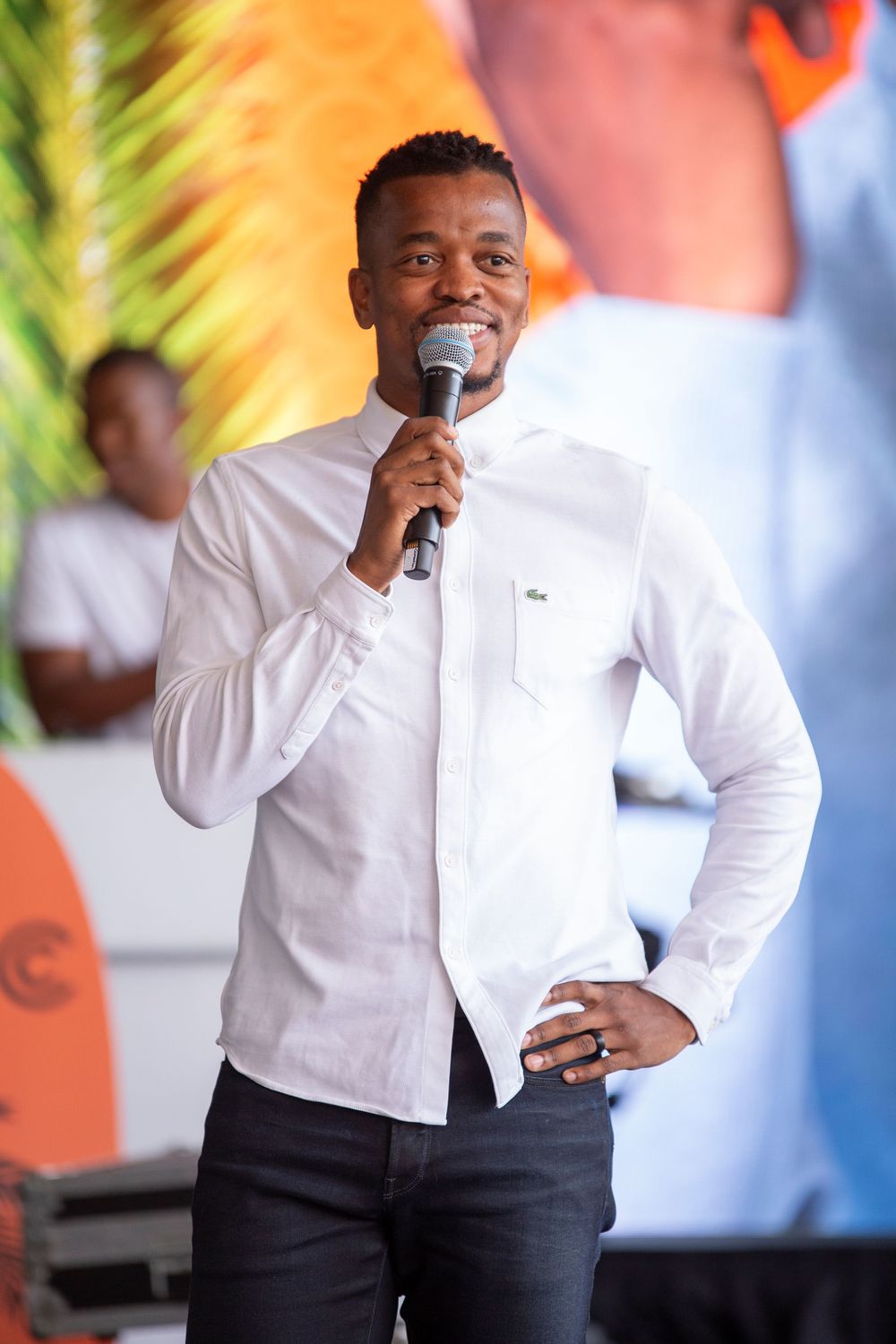 Singer performs with microphone wearing a crisp white long-sleeve shirt and dark pants on an outdoor stage.
