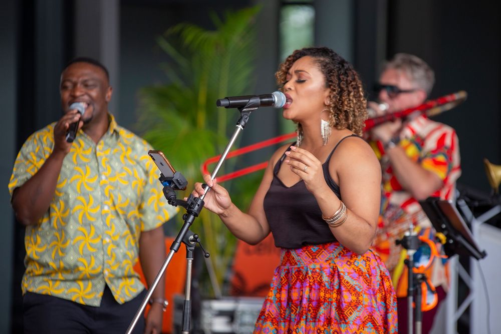 Musicians in vibrant yellow and red outfits perform energetically on stage with microphones and instruments.
