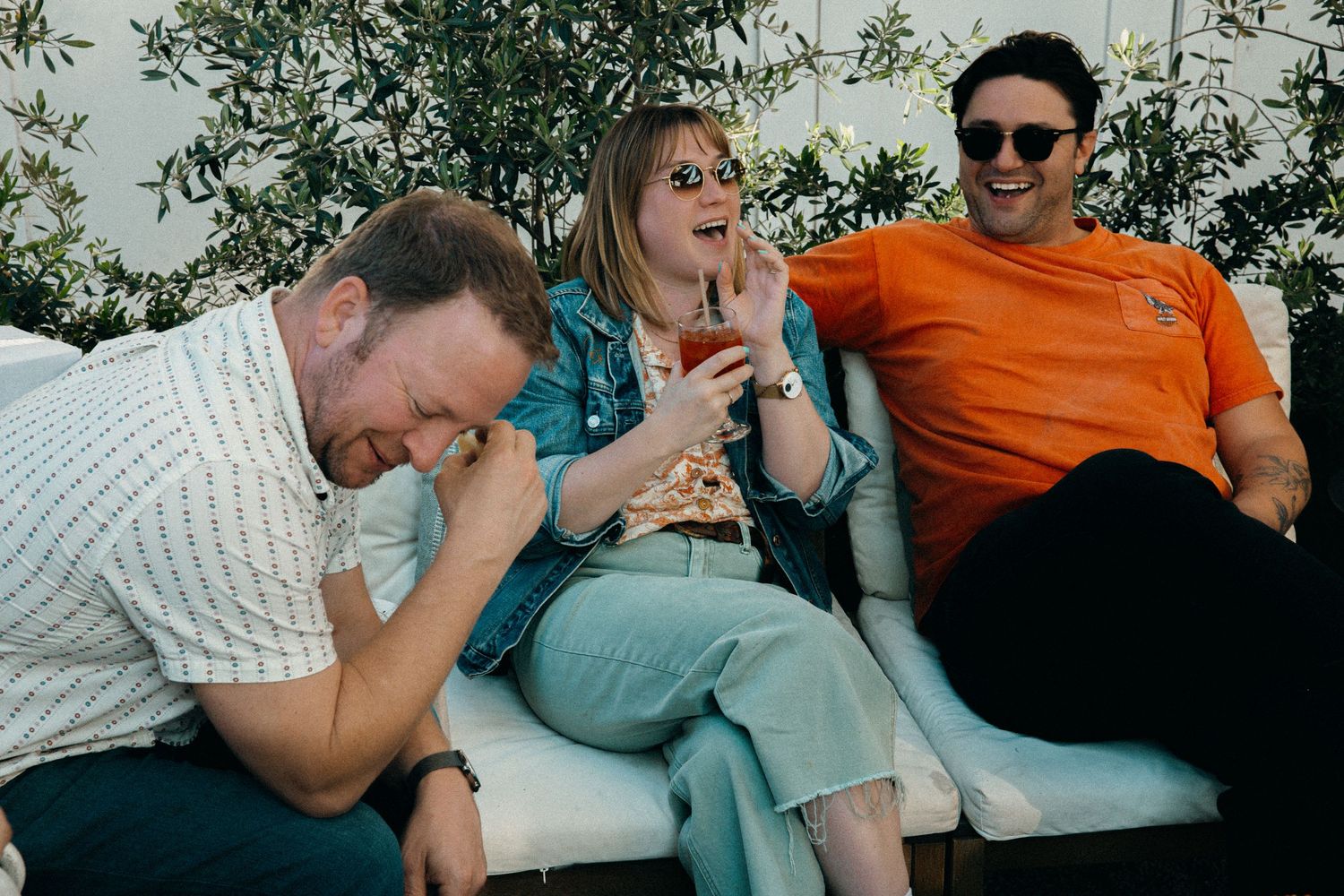 Group of friends relaxing outdoors on patio furniture during a sunny day.
