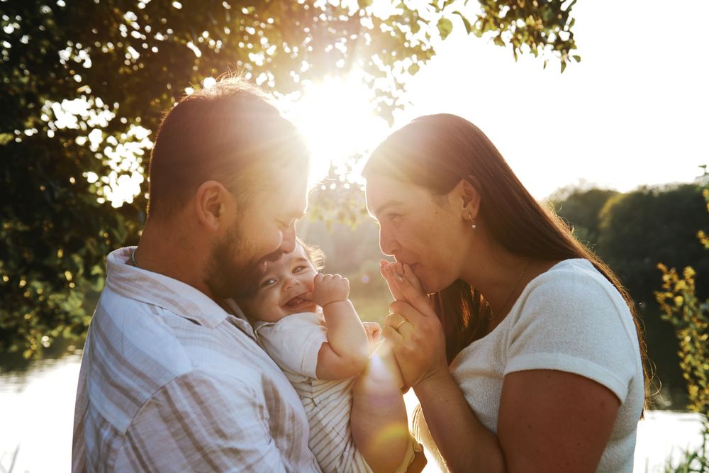 A young family with a baby enjoying a golden sunset outdoors near a lake, bathed in warm sunlight.