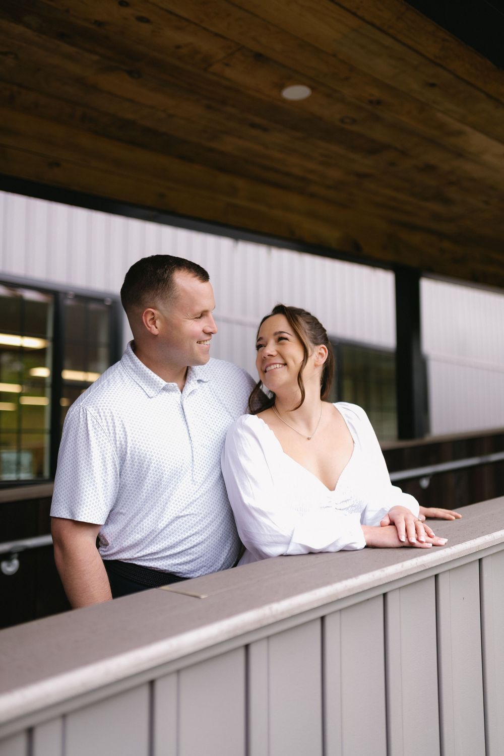 A couple shares a joyful moment together while leaning on a wooden balcony railing outside a building.