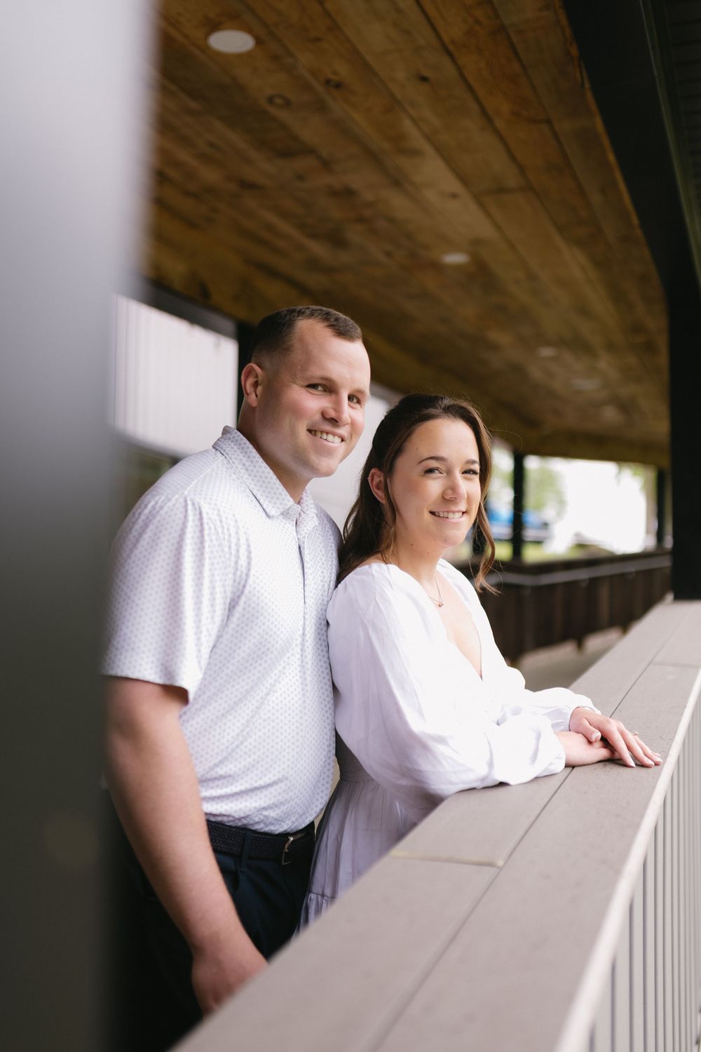 Couple in white outfits share sweet romantic moments as they lean on a white railing during an outdoor portrait session.