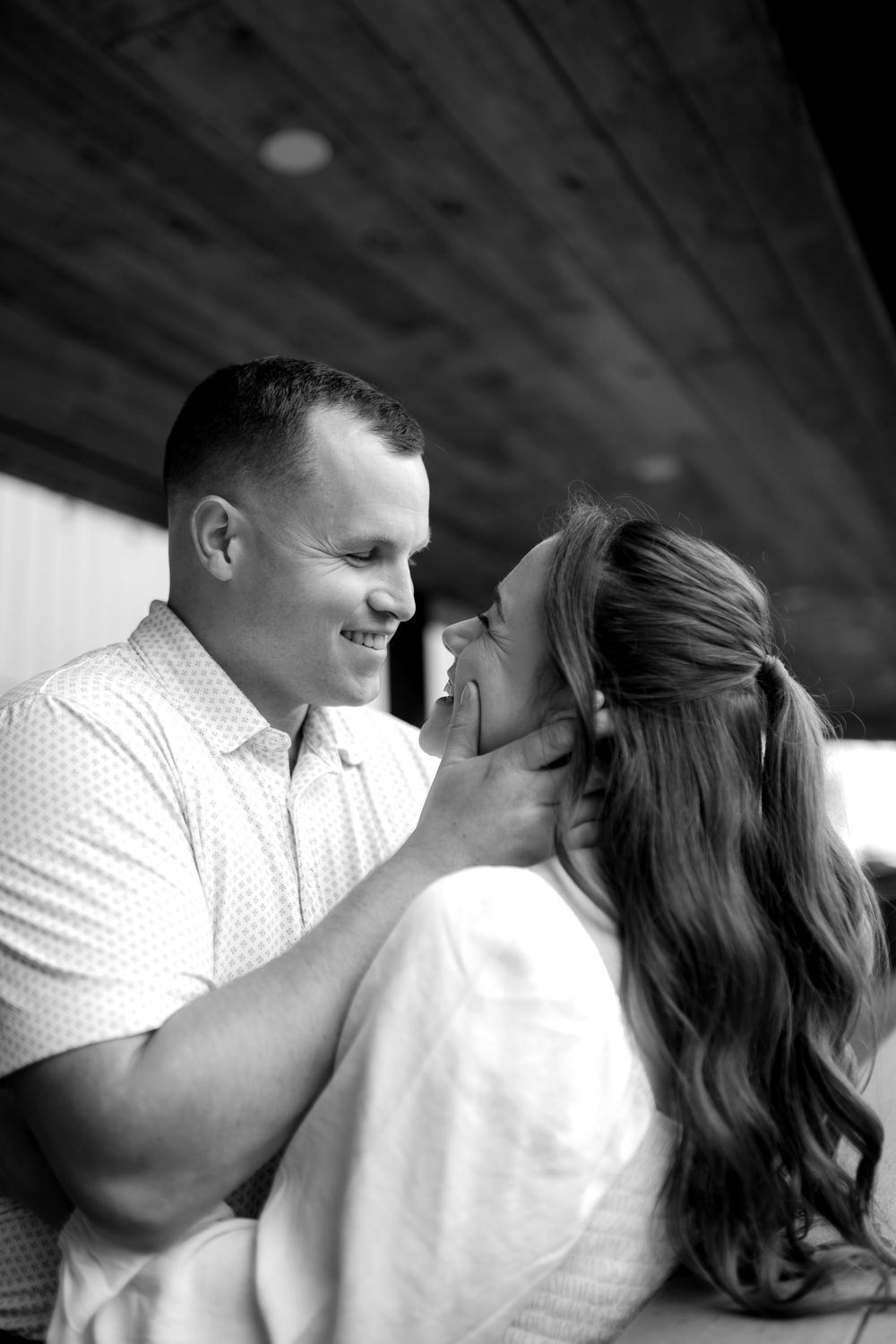 A black and white intimate portrait of a couple sharing a tender romantic moment underneath a wooden ceiling.