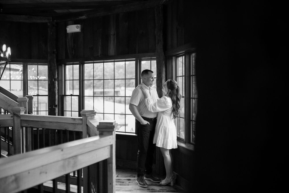Black and white photo of two figures embracing by large windows in an indoor space with wooden interior details.