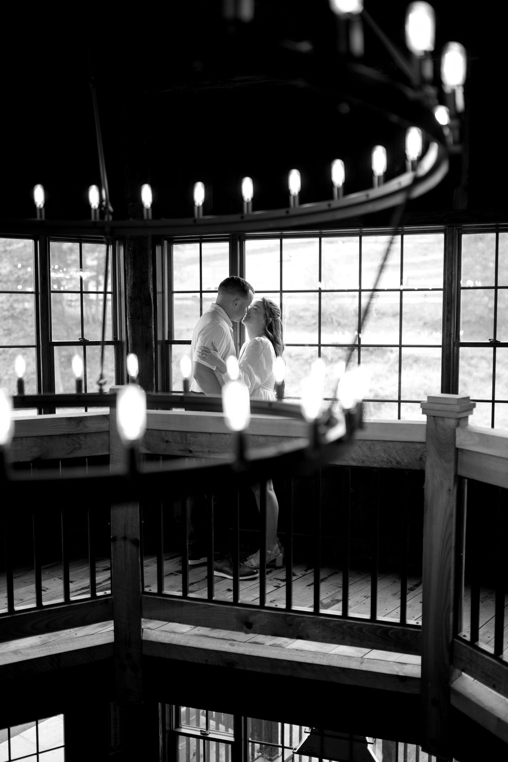 A silhouetted couple embracing in a circular stairwell with glowing lanterns illuminating the romantic black and white scene.