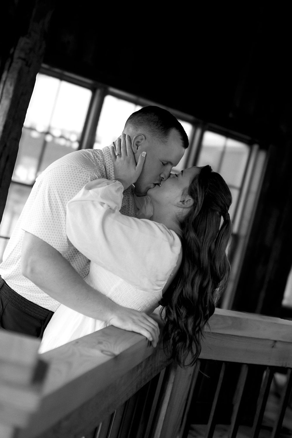 A romantic black and white portrait of a couple sharing a tender kiss on a porch.