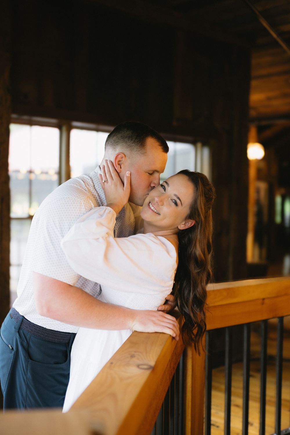 A romantic couple sharing an intimate moment at a rustic wooden railing while dressed in white and navy blue.