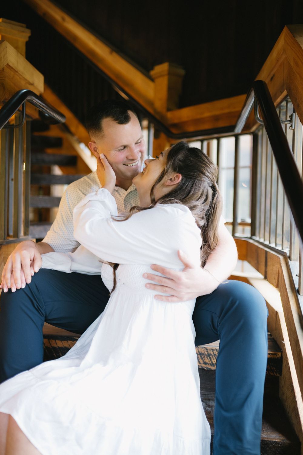 A tender embrace between a couple sitting on wooden stairs, dressed in white and dark colors.
