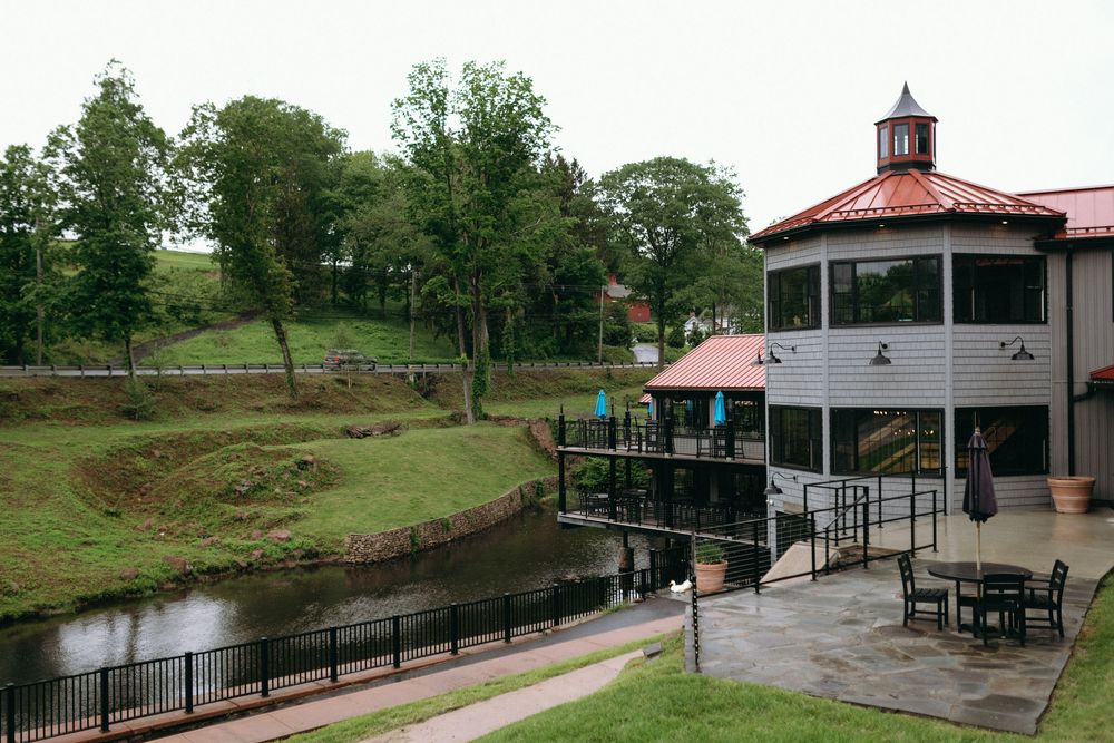 A riverside pavilion with a red cupola and outdoor seating area surrounded by green trees.