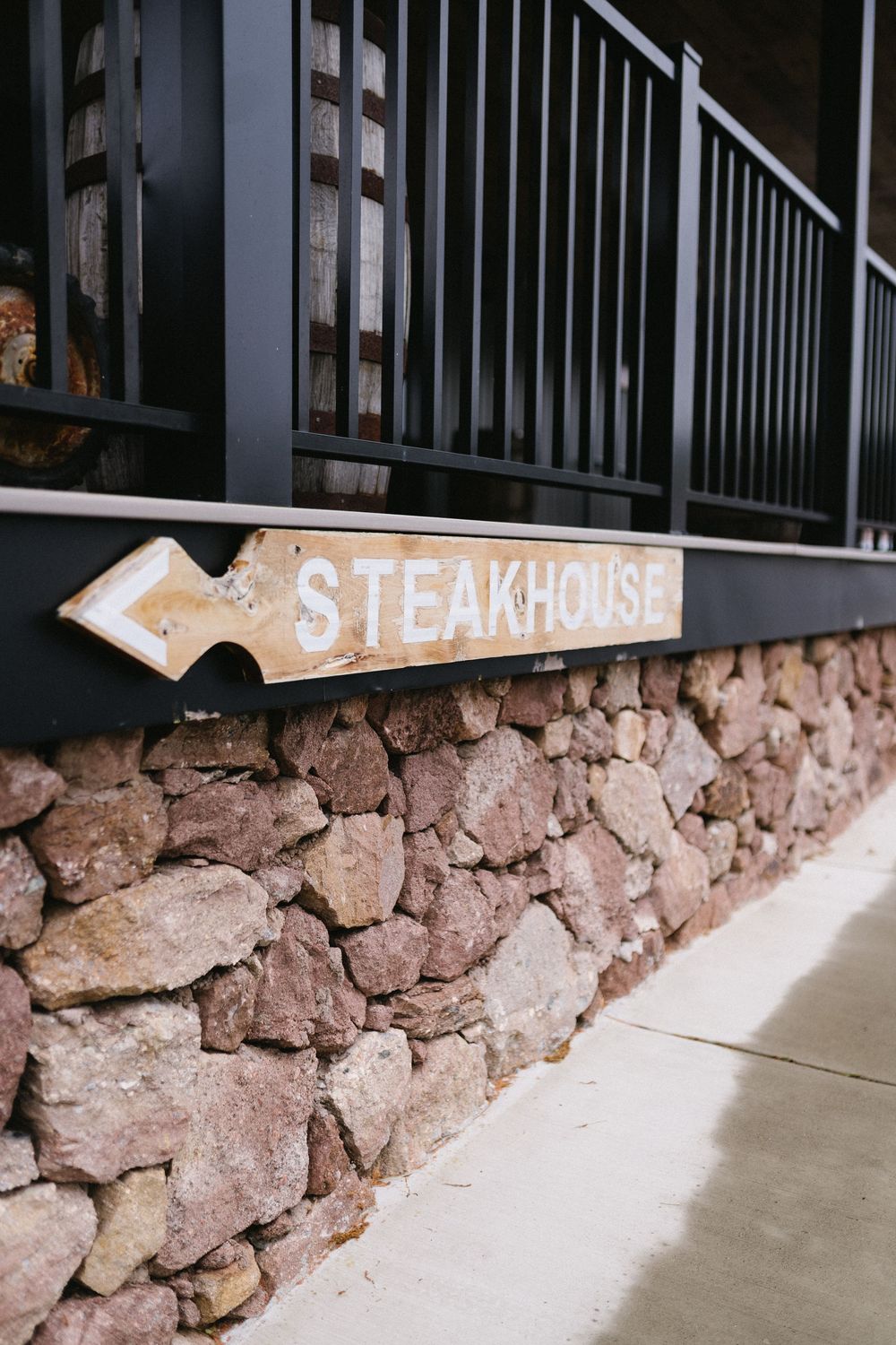 A rustic wooden arrow sign reading 'Steakhouse' mounted on a stone wall with metal railings above.
