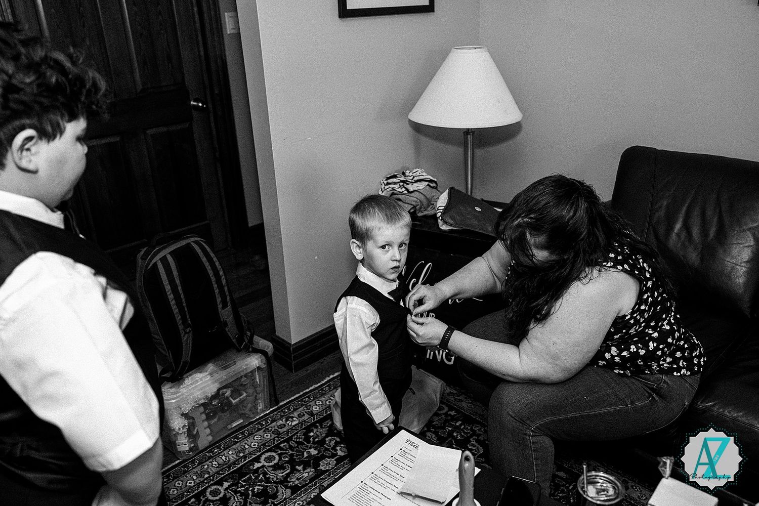 A candid black and white moment captured during a formal preparation scene showing adjustments being made to a young vest.