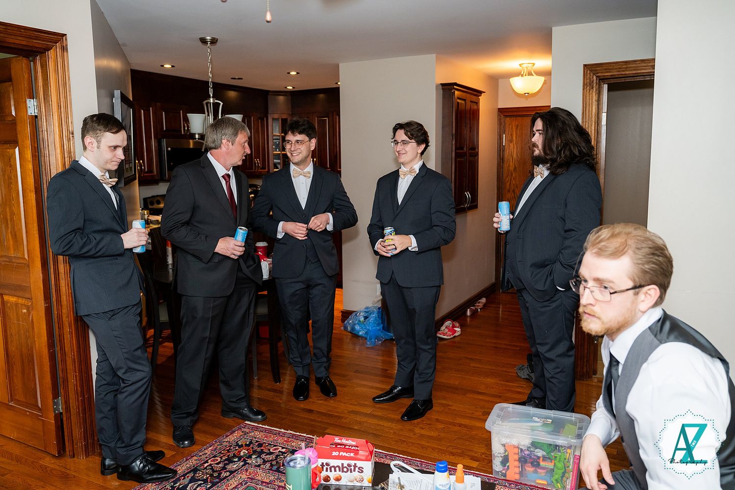 Several people in formal attire gather for a social event in an apartment living room with snacks and drinks.