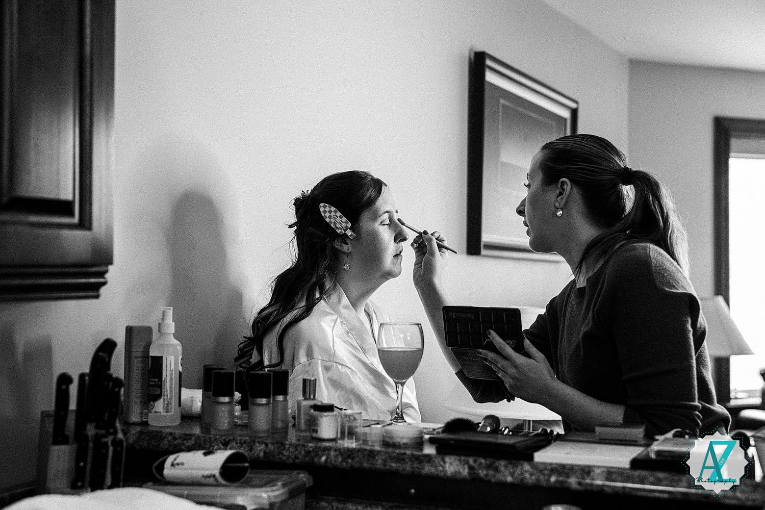 Black and white photo of a professional makeup artist applying cosmetics to a client at a beauty station.