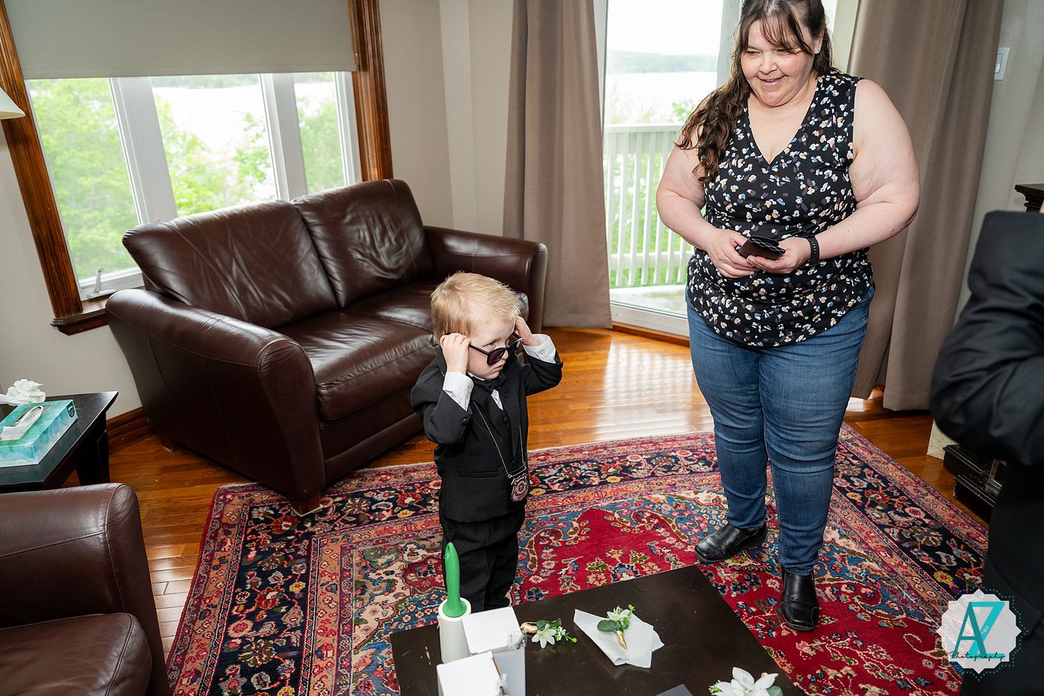 Young toddler stands playing with toys on an ornate traditional rug in a living room with leather furniture.