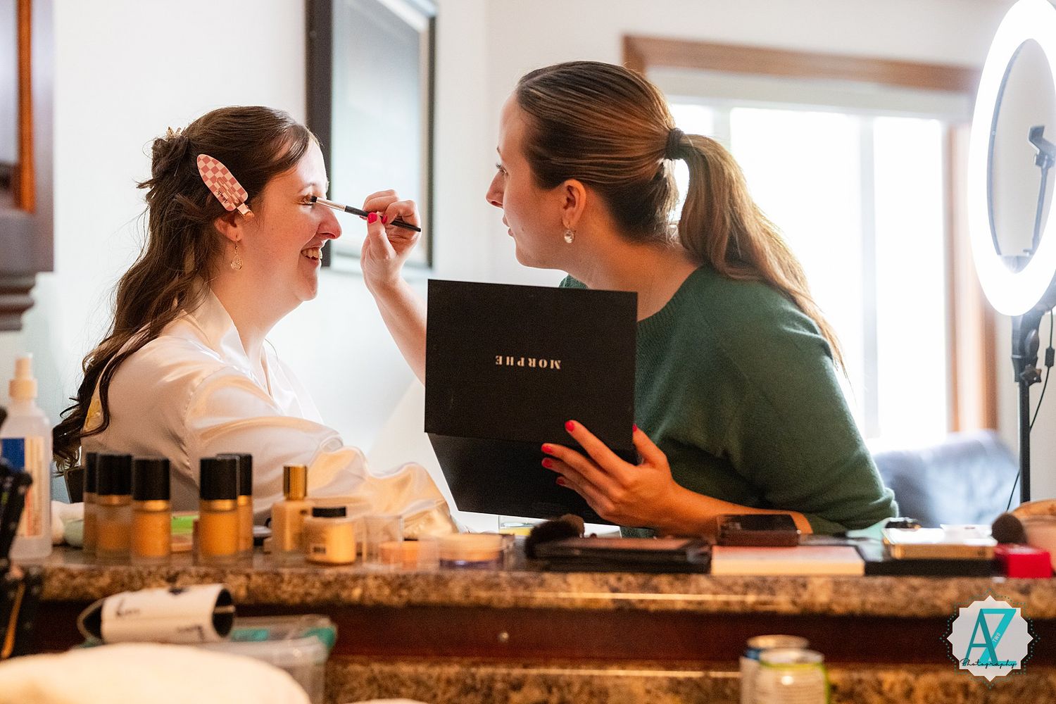 Professional makeup artist applying cosmetics to a client at a vanity table with beauty products displayed.