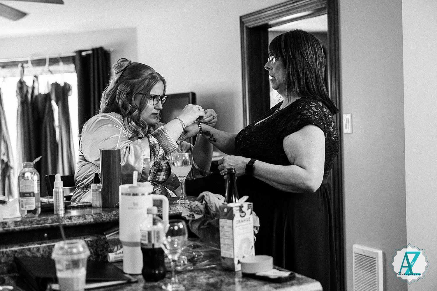 A black and white photo showing two people getting ready at a makeup vanity with hair styling tools and products.