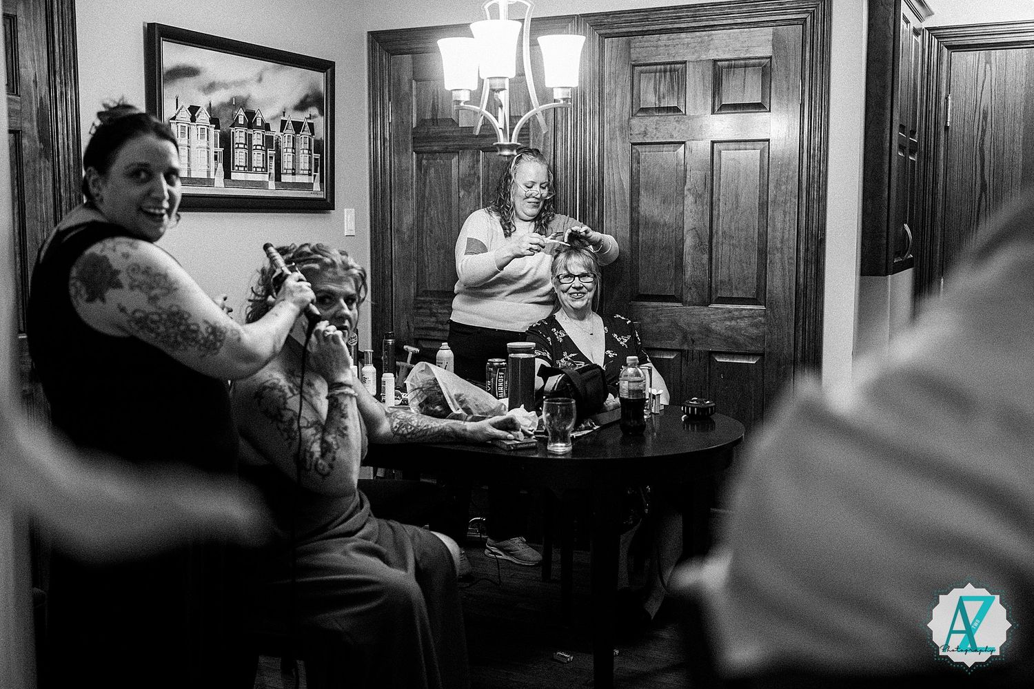 A black and white candid photograph shows people sitting around a table in a cozy, dimly lit wood-paneled room.