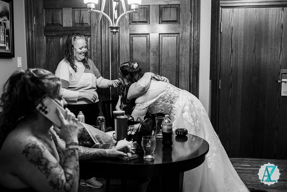A candid black and white wedding photograph capturing guests seated at a round table in a cozy, wood-paneled venue.
