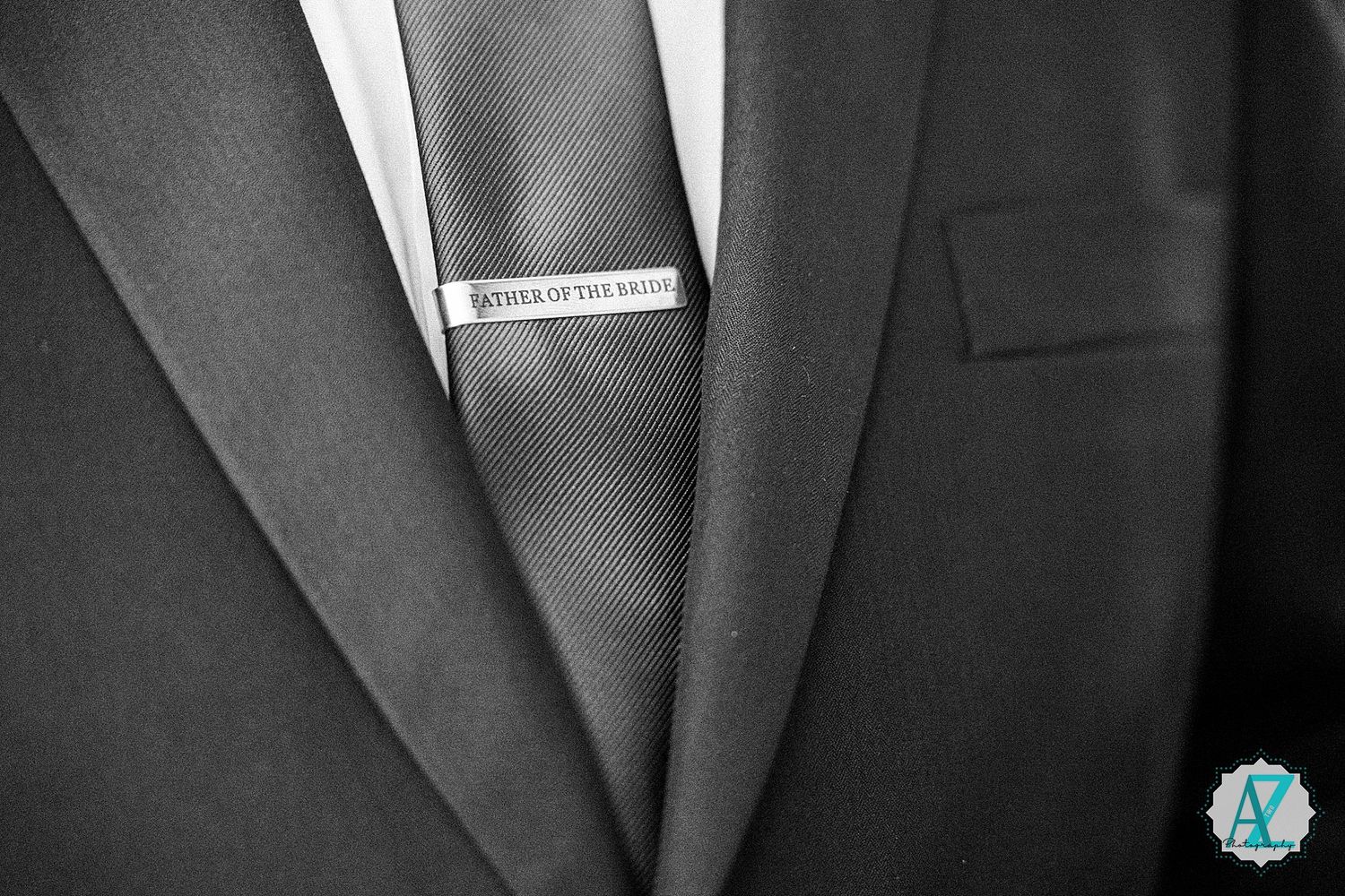 Close-up black and white photo of a formal suit jacket with a silver tie clip detail.
